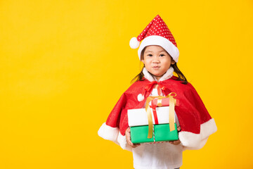Asian little cute girl smile and excited, Kid dressed in red Santa Claus hat hold gift box on hands concept of holiday Christmas Xmas day or Happy new year, studio shot isolated on yellow background