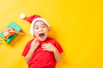 Asian little cute child boy smile, Top view of a kid dressed in red Santa Claus hat the concept of holiday Christmas Xmas day or Happy new year, isolated lying on yellow background