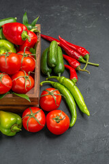 Side view of fresh vegetables inside and outside of a brown wooden basket on the right side on dark background in vertical view