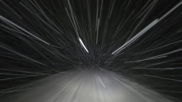 Drive by car at night on a winter forest road in snowfall. Heavy snow is reflected in the light of the car headlights. Travel in winter by car