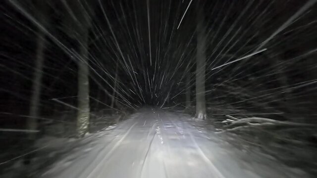 Drive by car at night on a winter forest road in snowfall. Heavy snow is reflected in the light of the car headlights. Travel in winter by car