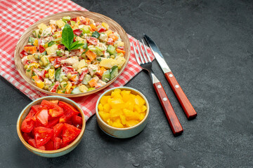 side close view of bowl of vegetable salad on red napkin with veggies and cutleries on side and with free place for text on dark table