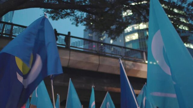 Inner Mongolian People's Party And Uyghuristan Flags Fluttering In The Wind Held By Protesters Against CCP In Tokyo, Japan At Night. - low angle shot