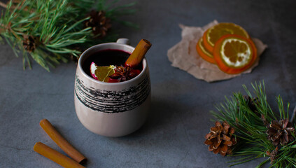 Mulled wine in a dark background with cinnamon and a slice of orange surrounded by pine branches. Winter drink.