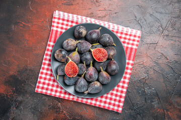 Above view of full fresh black mission figs split ones on a black plate on red stripped towel on colorful table