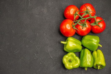 Top view of fresh vegetables red tomatoes with stems and green peppers necessary for cooking on dark background