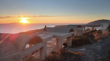 Aerial shot of a parkour traceur running over a building and doing a flip at sunrise in Santorini - Powered by Adobe