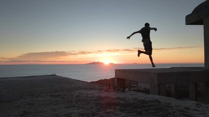 Slow motion shot of a man jumping between roofs practicing parkour at sunrise - Powered by Adobe