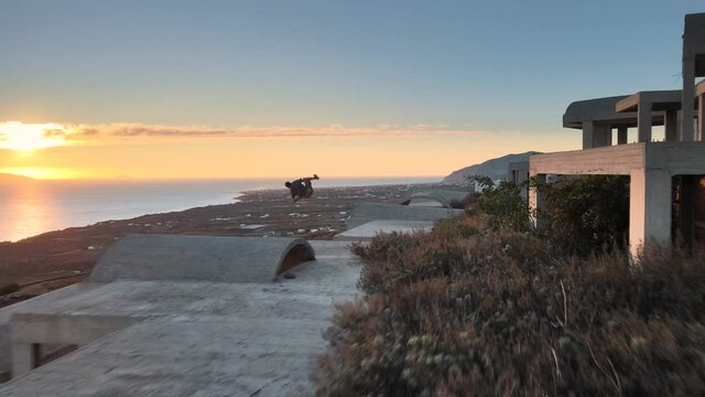 Aerial shot of a parkour traceur running and doing flips on a building in Santorini at sunrise