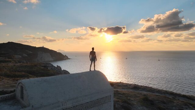 Aerial parallax shot of a man looking at sunset from the roof of a building in Santorini