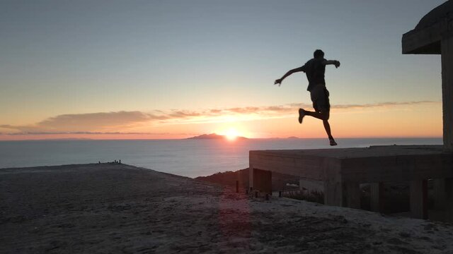 Slow motion shot of a man jumping between roofs practicing parkour at sunrise
