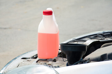 Under the open hood of the car is a white canister of pink liquid. fluid replacement.