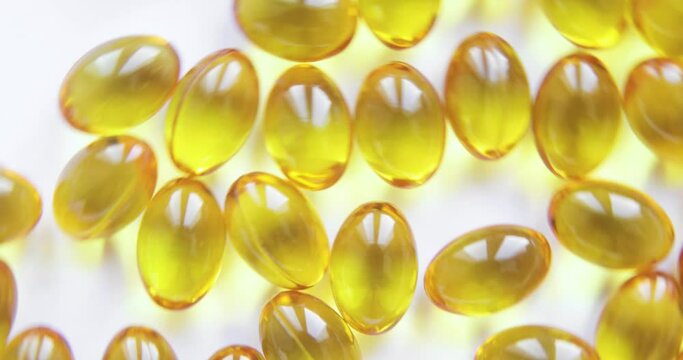 Beautiful small oval transparent gel capsules with yellow oily liquid inside. Pills are rotating on white background. Organic supplements vitamins, yellow capsules of Omega 3 or D 3 pills.