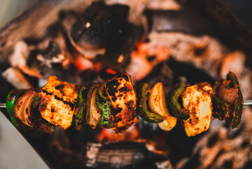 Selective focus on Indian spicy cottage cheese in barbeque on charcoal fire. Spicy paneer tikka with onion and capsicum char-grilled on coal flames. Top view of appetizer food on BBQ.