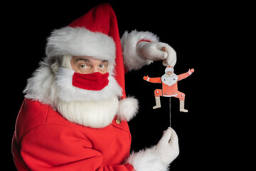 Man in santa costume and mask image puppet in the hands of Santa black background.
