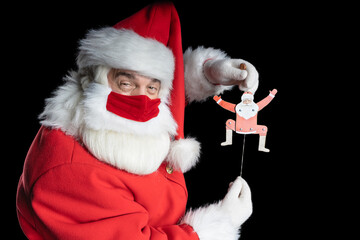 Man in santa costume and mask, with sly eyes image puppet in the hands of Santa black background.