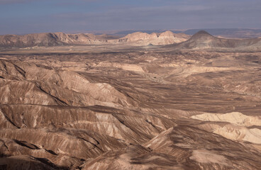 Fototapeta na wymiar Majestic mountain range in a remote part of Negev desert, Israel. Panoramic landscape of dry wadies, colorful sandy hills, mountain folds and rock formations. The harsh beauty of the desert.
