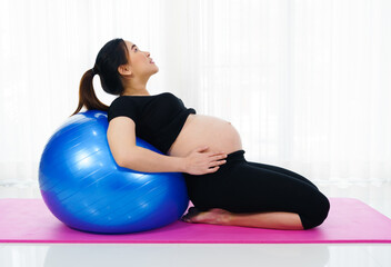Fototapeta premium pregnant woman doing yoga exercise on fitness ball in living room at home