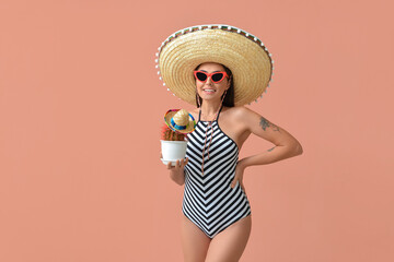 Beautiful young woman in swimsuit and sombrero hat holding cactus on color background