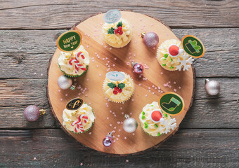 Board with tasty Christmas cupcakes on wooden background