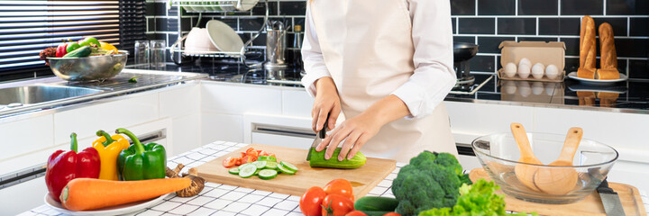 young Asian woman is preparing healthy food vegetable salad by Cutting cucumber for ingredients on cutting board on light kitchen, Cooking At Home and healthy food concept.