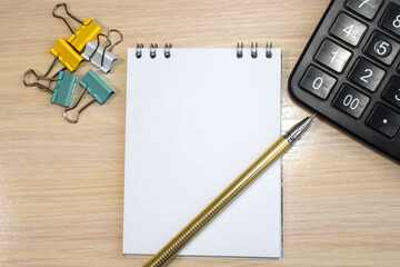 on the wooden table is a notebook with a pen near the calculator and stationery clips. Concept photo