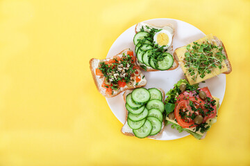 Fototapeta na wymiar Toasts, sandwiches with cucumbers, tomatoes, eggs, sprouts, herbs and nuts on a plate on a yellow background. Vegetarian food concept. Copy space.
