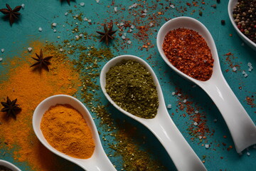 Various colorful herbs and spices for cooking in spoons. Pepper, chili, paprika, basil, turmeric.