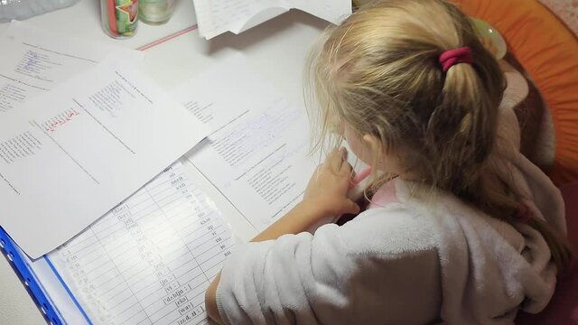 A little girl getting ready for school doing homework school lessons. Writes in notebooks sitting at a special school table in the children's room