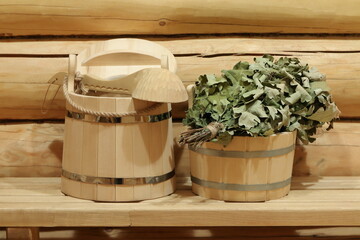 Wooden bucket, ladle and oak broom are on a bench in sauna. 