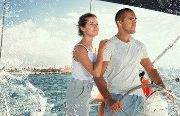 Young loving couple standing at yacht wheel enjoying sea trip along coast of Barcelona on sunny day © JackF
