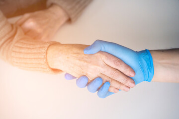 Handshake, caring, trust and support. A doctor's hand in a blue glove holds the hand of an elderly woman, a patient. Medicine and healthcare.