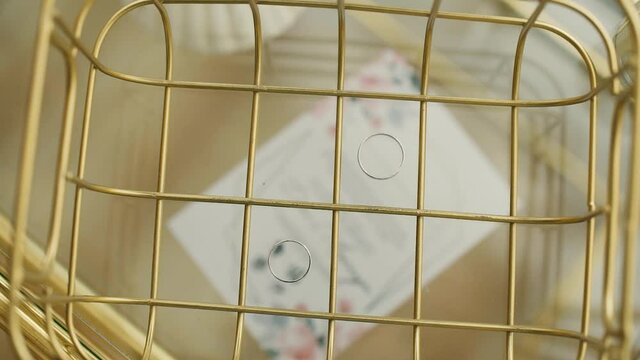 Two wedding rings are in a gold cage in different cells on the background of the silhouette of a wedding invitation card