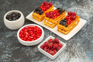 bottom view berry waffles on white rectangular plate bowls of pomegranates raisins and raspberries on grey-white background