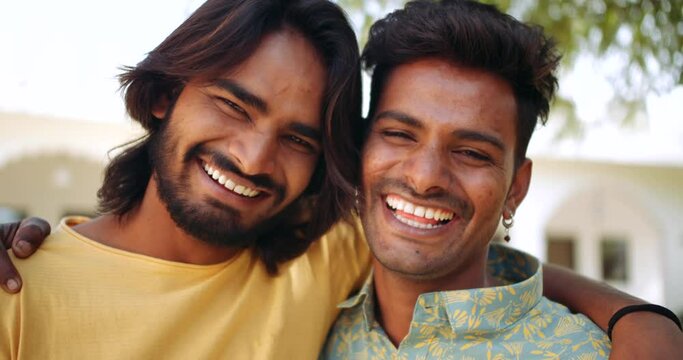 Portraits of two male best friends hugging with arms around pointing fingers happy smiling making fun joke looking at camera pov