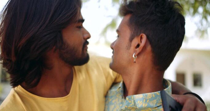 Portraits of two male best friends hugging with arms around pointing fingers happy smiling making fun joke brothers lovers togetherness happy in building exterior 