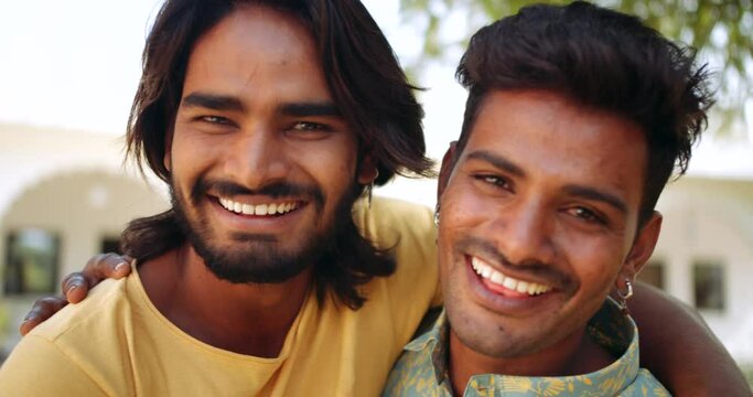 Portraits of two male best friends hugging with arms around pointing fingers happy smiling making fun joke brothers lovers togetherness happy in building exterior 
