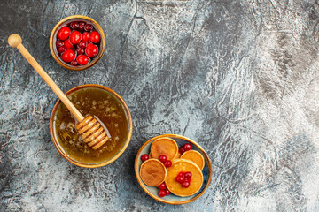Fruit pancakes with red cornel berries in a bowl and honey with wooden spoon on dark table