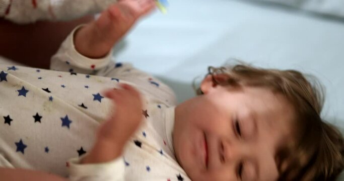 Mother trying to brush baby toddler teeth before sleep. Infant refusing toothbrush