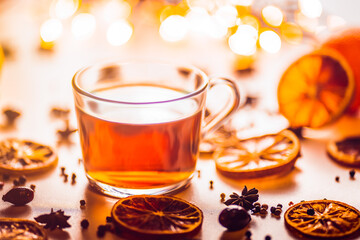Glass cup of hot aromatic tea on white background with spices. Christmas tea with oranges on bokeh lights background. Christmas tea.	