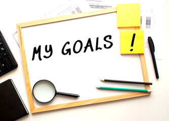 MY GOALS text is written on a white office board. Work table with office supplies.
