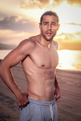 Fitness man standing on the beach without shirt. Athletic fit male shirtless. Showing abs. Personal trainer posing.
