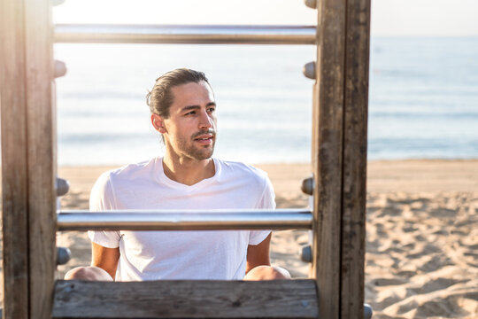 Male firness personal trainer working out at the beach using bars and bench.