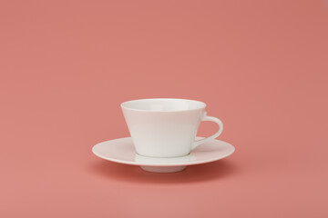 White ceramic tea or coffee cup on a plate on dirty pink background with space for text