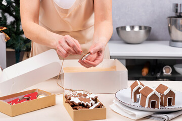 Woman wrapping christmas gingerbread cookies in holiday boxes
