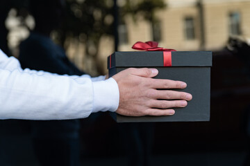 Black gift box with red bow in male hands on black background. Holidays