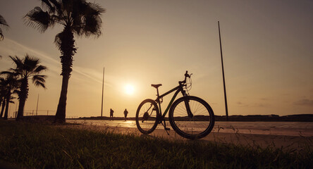 Fototapeta premium Silhouette of a bike at sunset. The sun shines through the bicycle wheel at sea side park