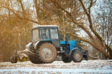 Tractor with rotating brush clears road in city park from fresh fallen snow in cold winter day....