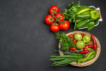 Two vegetable baskets with a bunch of green and peppers cucumber and tomatoes with stem on dark background