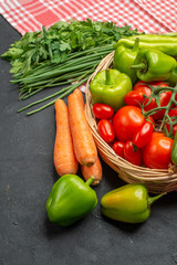 Vertical view of fresh various organic vegetables in a wooden basket on orange stripped towel on dark background